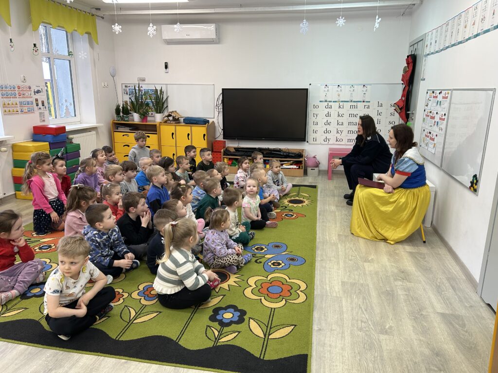Wszystkie przedszkolaki siedza na dywanie w sali i rozmawiają z zaproszonymi gośćmi ważnych informacji dotyczących BEZPIECZNYCH FERII i przestrzegania ZASAD DOTYCZĄCYCH NASZEGO ZDROWIA.