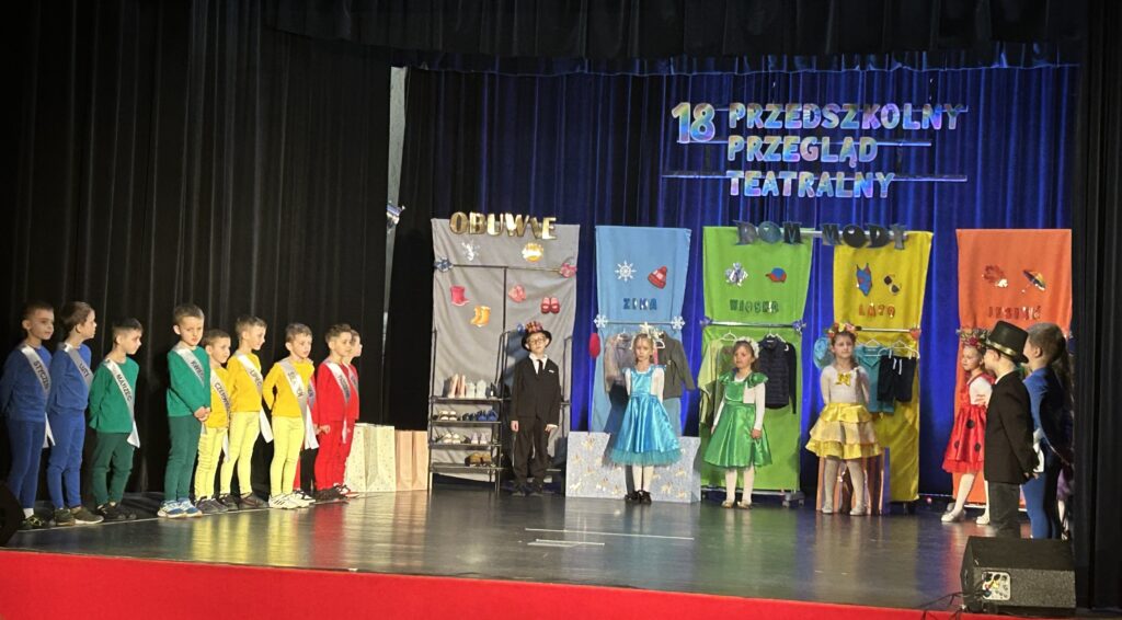 Zdjęcie przedstawia dzieci z grupy starszej stojące na scenie i występujące jako aktorzy w przedstawieniu o miesiącach i modzie. 