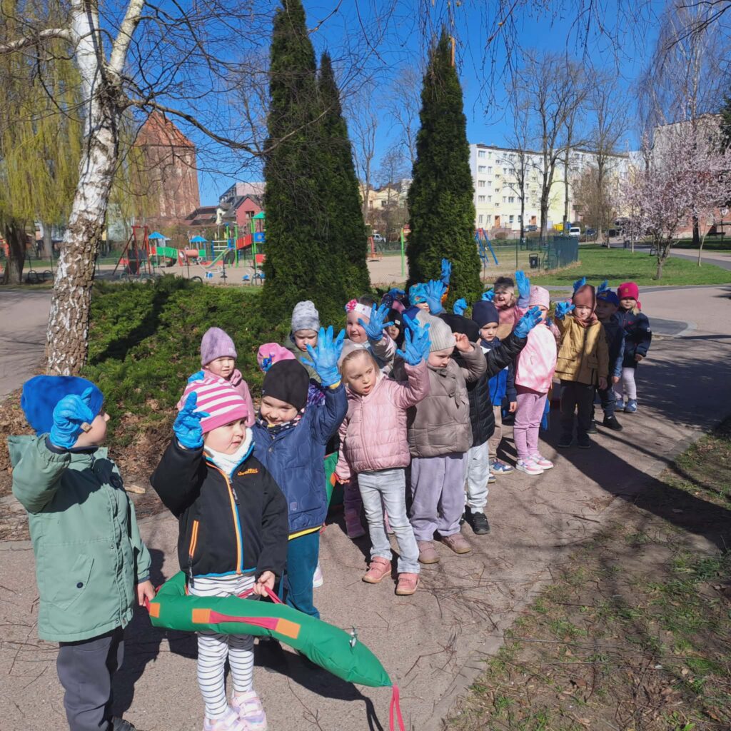 zdjęcie przedstawia przedszkoalki na spacerze, ktore na ręku maja zalożone rękawiczki jednorazowe i będą za chwilę zbierały śmieci w parku z okazji DNIA ZIEMI 