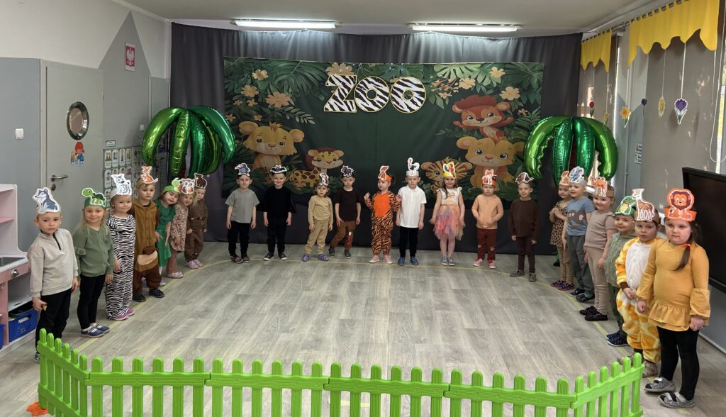 dzieci przygotowane do występu stoją w sali przedszkolnej przed dekoracją i w specjalnych strojach, maskach , ozczekują na swój występ pod tytułem IDZIEMY DO ZOO