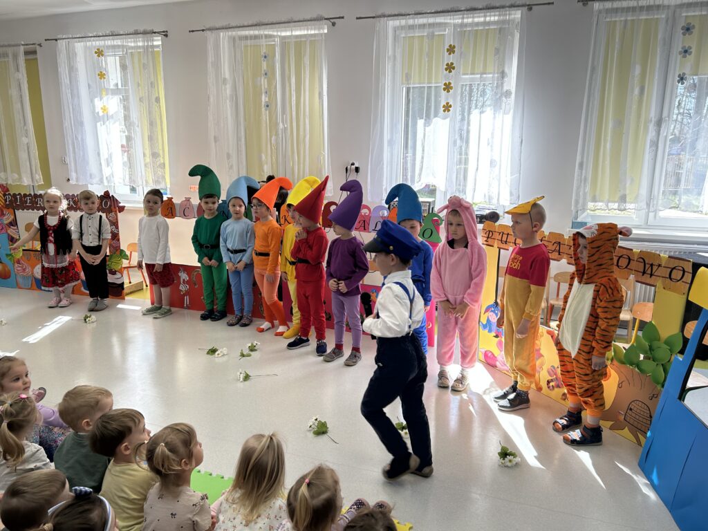 Zdjęcie przedstawia dzieci ubrane w strojach bohaterów z bajki które występuja przed innymi przedszkolakami w przedstawieniu ZACZAROWANY POCIĄG