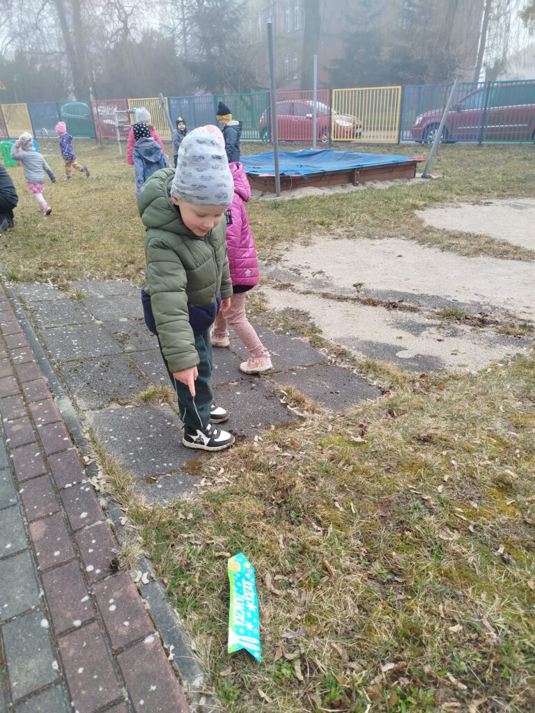 Przedszkolaki uczesnicza w zabawie zorganizowanej w przedszkolnym ogrodzie dotyczącej wielkiej Nocy. Tradycja nakazuje szukac jajek, wieć dzieci szukaja ich ukrytych w trawie