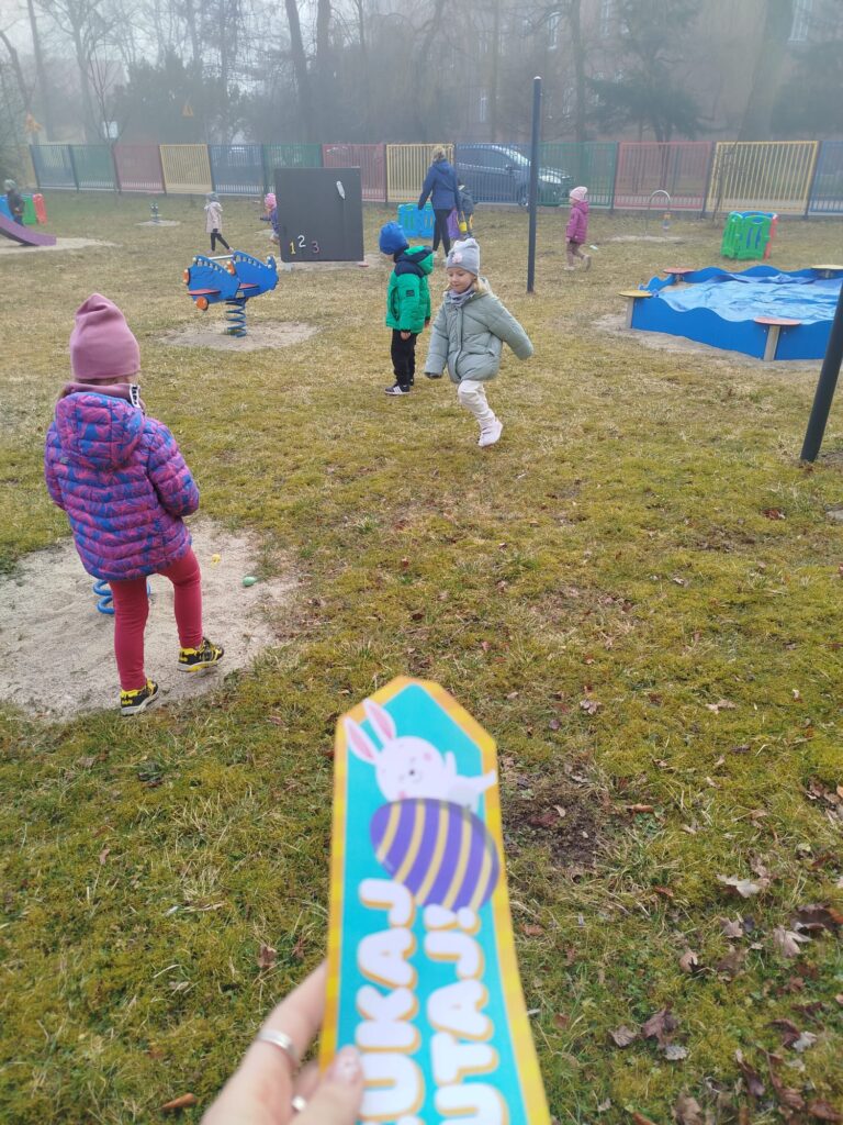 Kazde dziecko biega w przedszkolnym ogrodzie i szuka jajek ukrytych w trawie zeby dostać od zajączka prezent