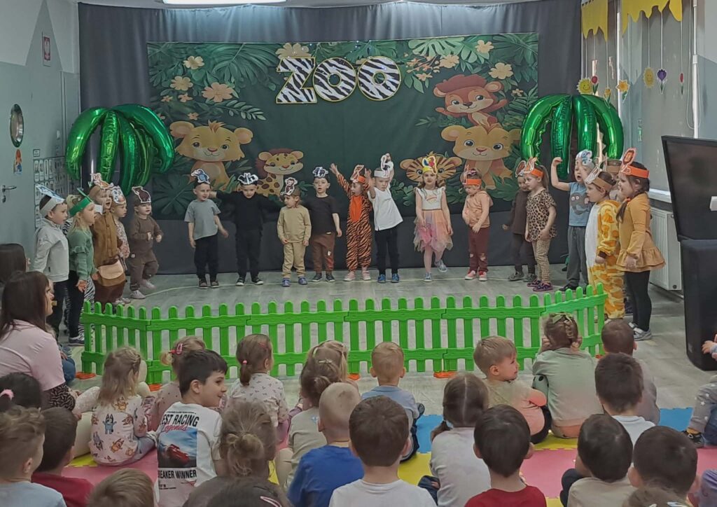 dZIECI WYSTĘPUJA W PRZEDSTAWIENIU O ZWIERZĘTACH Z ZOO. STOJA PREZENTUJĄC SIĘ NA SCENIE PRZED INNYMI PRZEDSZKOLAKAMI 